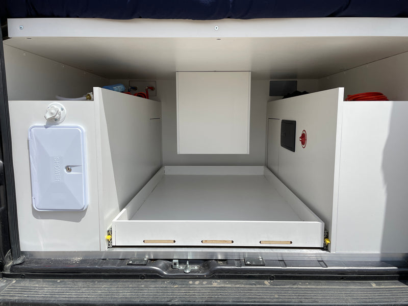 Inside an RV rental: rear utility area with pull-out storage, outdoor shower, and visible plumbing/electrical connections. — photo 10