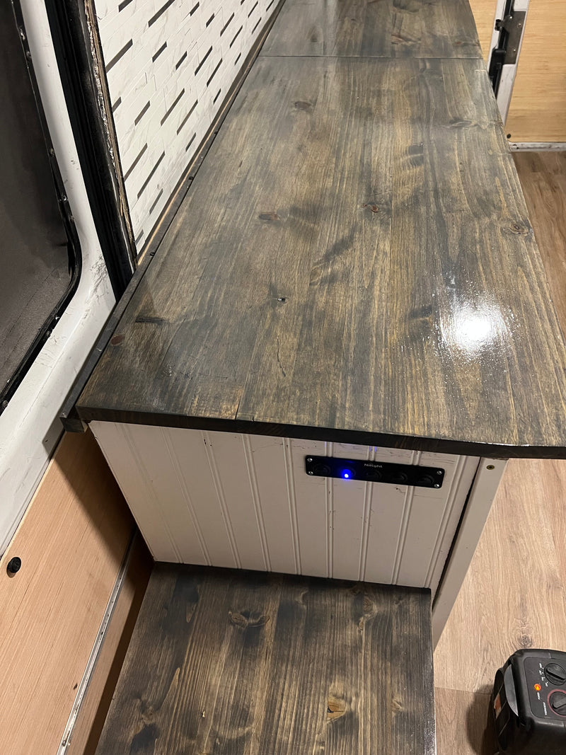 RV rental interior featuring a custom wood counter, white cabinet with controls, and wall paneling. — photo 7