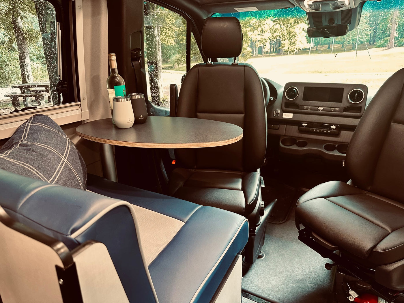 Cozy RV rental interior with blue seating, a table with drinks, and comfortable front seats, viewing a rainy park. — photo 5