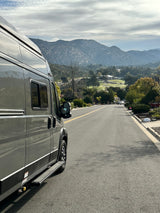 A grey RV rental van overlooks scenic mountains, a lush valley, and a golf course, ready for adventure.