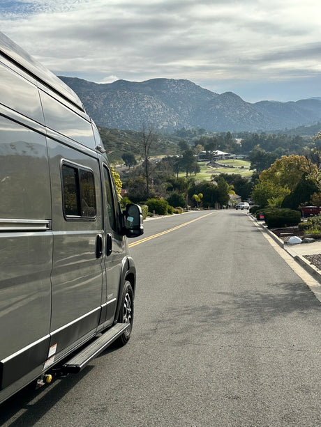 A grey RV rental van overlooks scenic mountains, a lush valley, and a golf course, ready for adventure.