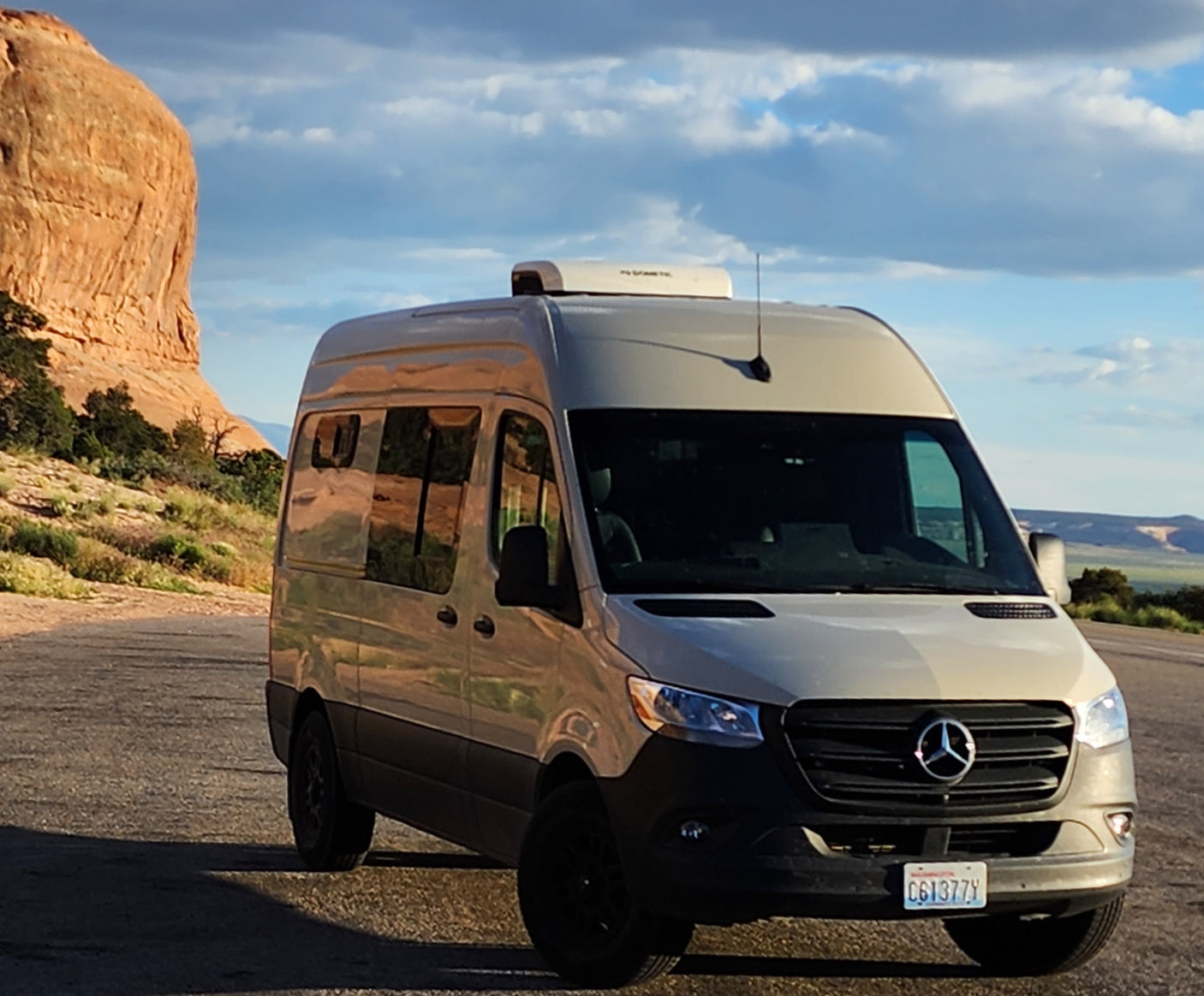 RV rental: Beige Mercedes Sprinter camper van on a desert road, by a large rock formation.