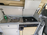 Compact RV rental kitchen with sink, two-burner stove, and refrigerator. Ideal for road trips.