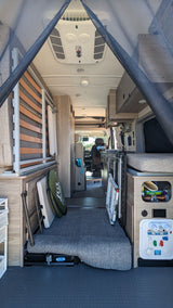 Organized RV rental interior showcasing a bed, smart storage solutions, and a utility panel for comfortable travel.