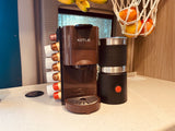 RV rental kitchen: KOTLIE coffee machine, pods, and frother on a countertop, with fruit nearby.