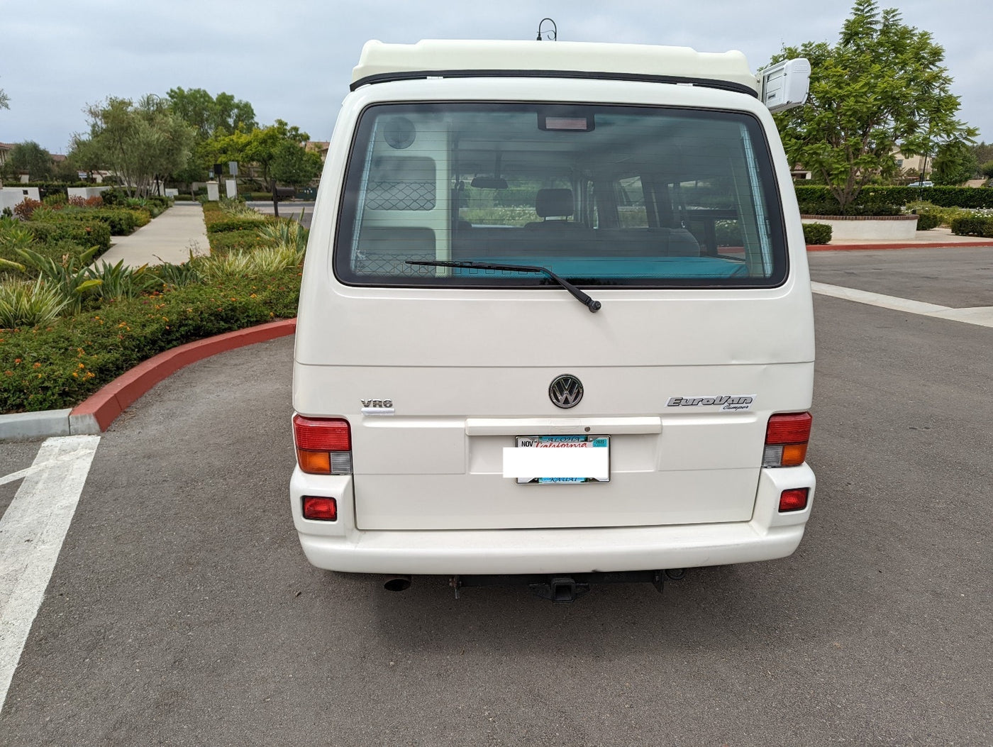 White Volkswagen EuroVan Camper's rear view, a great option for an RV rental. Parked on asphalt with landscaping, featuring a Hawaiian plate. — photo 4