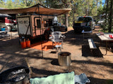 Relaxing RV rental campsite with a NO BO travel trailer, truck, fire pits, and outdoor seating under an awning.