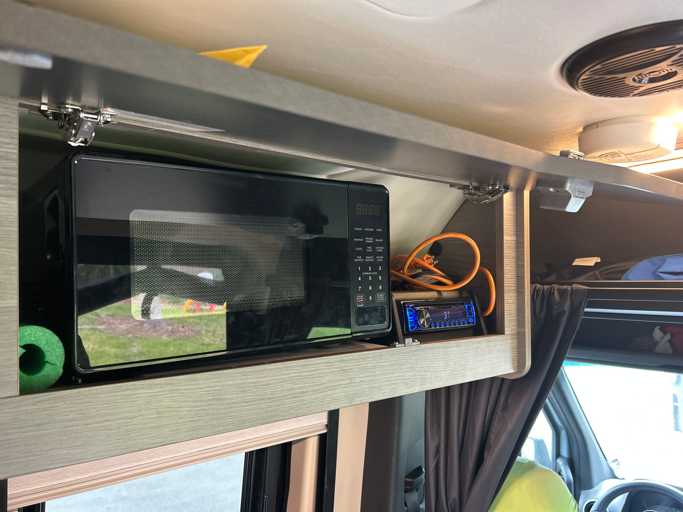 Compact RV rental kitchen setup featuring a built-in microwave, BOSS Bluetooth stereo, and overhead storage.