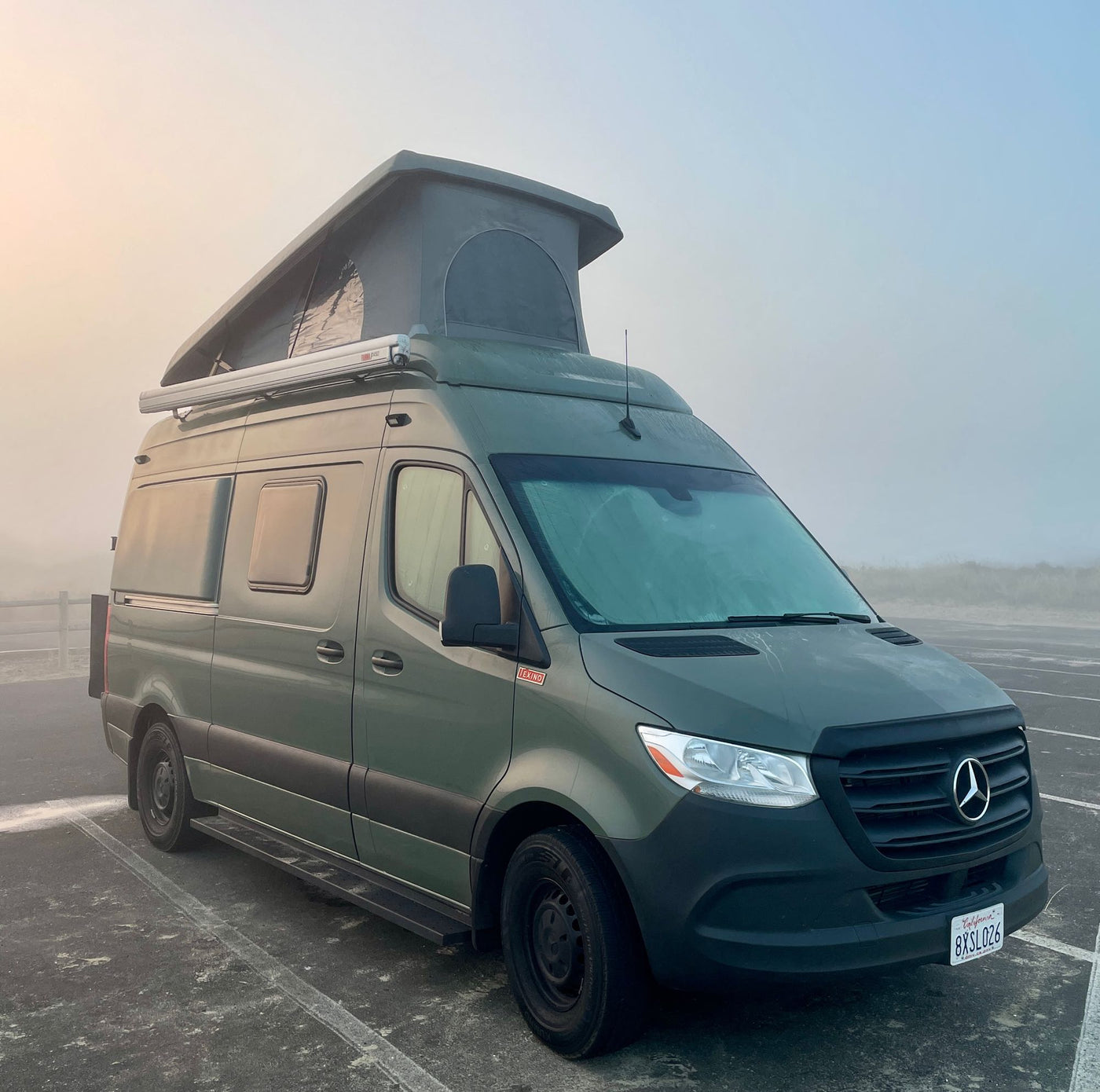 Green Mercedes-Benz Sprinter camper van, an ideal RV rental, parked in a foggy outdoor lot.