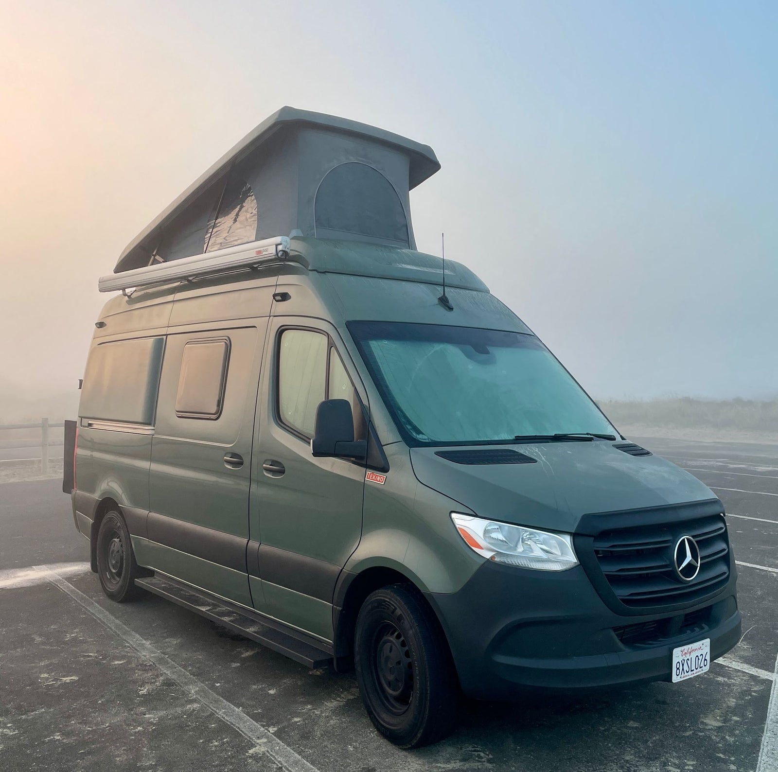 Green Mercedes-Benz Sprinter camper van, an ideal RV rental, parked in a foggy outdoor lot.