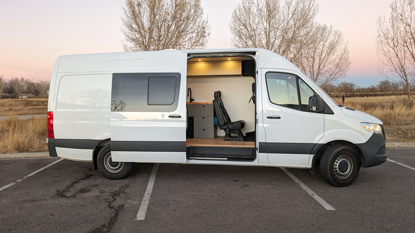 White conversion van RV rental, side door open to modern interior, parked at sunset. Ideal for mobile living.