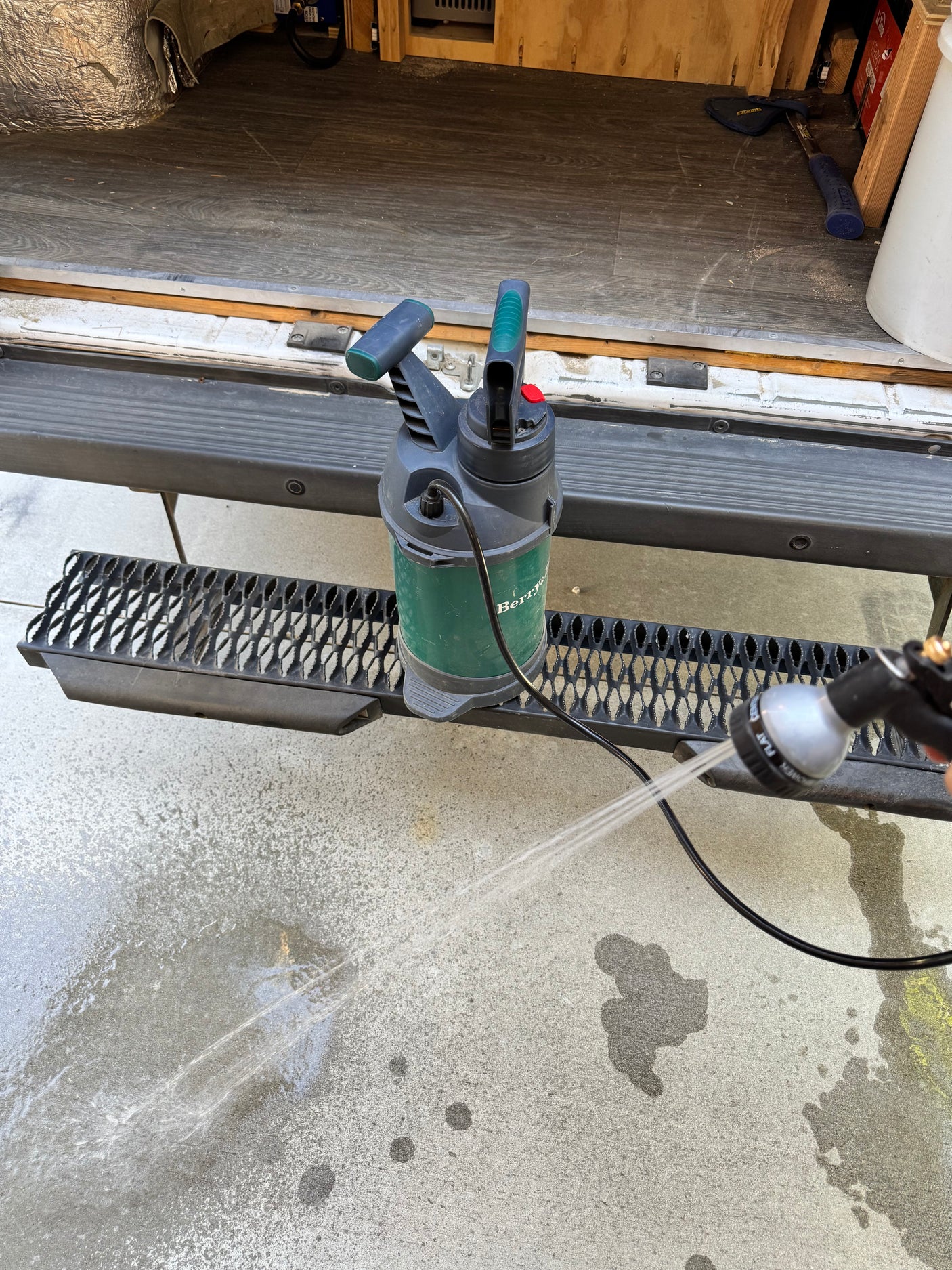 A portable sprayer on an RV rental's rear step sprays water onto the ground, ideal for cleaning gear.