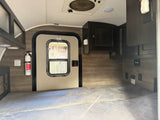Inside a cozy rv rental: a bed, door, fire extinguisher, and overhead cabinets, ready for your next travel adventure.