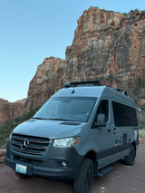 Adventure awaits with this sleek grey Mercedes Sprinter RV rental, parked against stunning red rock mountains.