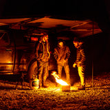 Night camping under an RV rental awning. Three men gathered around a cozy fire pit, enjoying the outdoors.