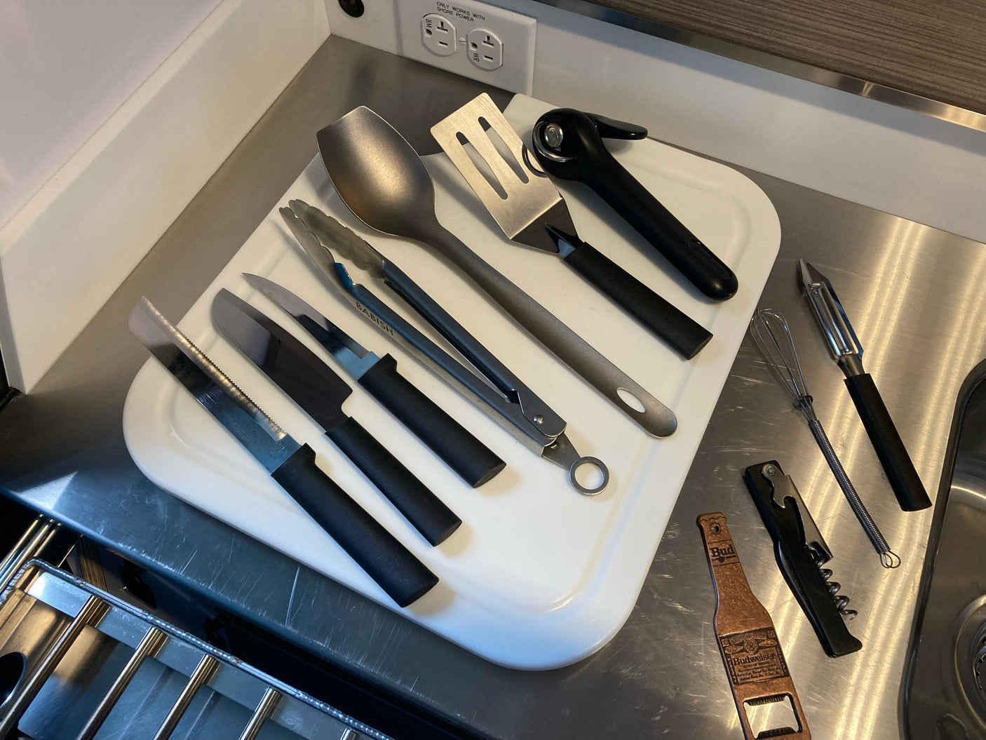 Essential kitchen tools for your RV rental: knives, spatulas, tongs, can opener, and more on a cutting board.