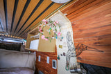 Personalized rv rental interior featuring custom wood paneling, a creative jewelry display, and cozy bed area.