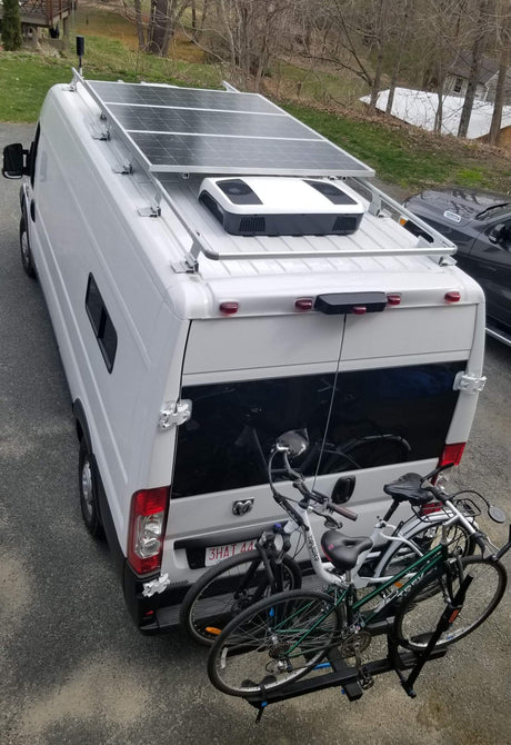 This white RV rental camper van features rooftop solar panels, AC, and a bike rack, ideal for road trips and adventure.
