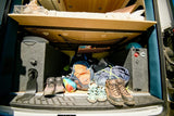 RV rental storage: Organized camper van trunk showing bed, outdoor gear, hiking boots, and power station for adventures.