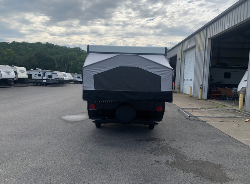 This Flagstaff pop-up camper, a great RV rental option, is shown from the rear in a lot with other travel trailers and a service building. — photo 2