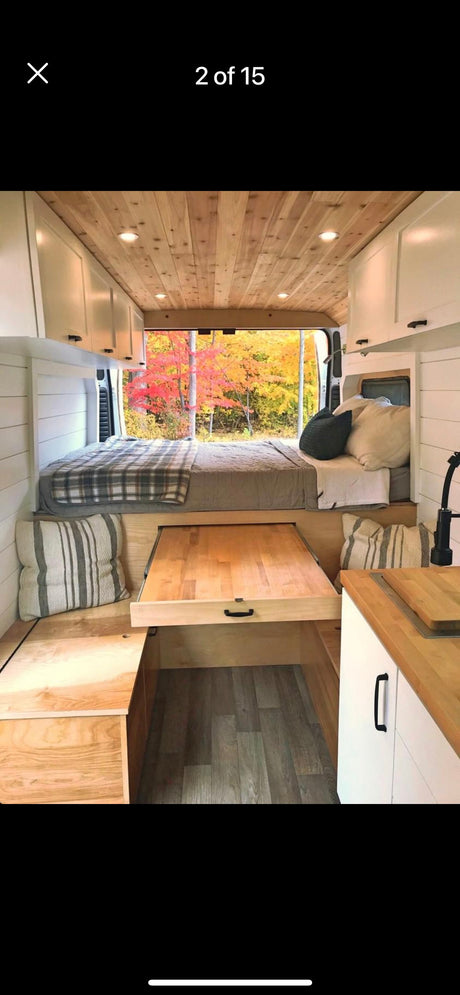 Spacious RV rental interior featuring a cozy bed, pull-out table, kitchen, wood ceiling, and stunning autumn views.