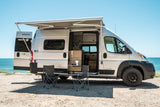 Coastal rv rental: Winnebago Solis Pocket camper van with awning, chairs & coffee setup by the sunny ocean.