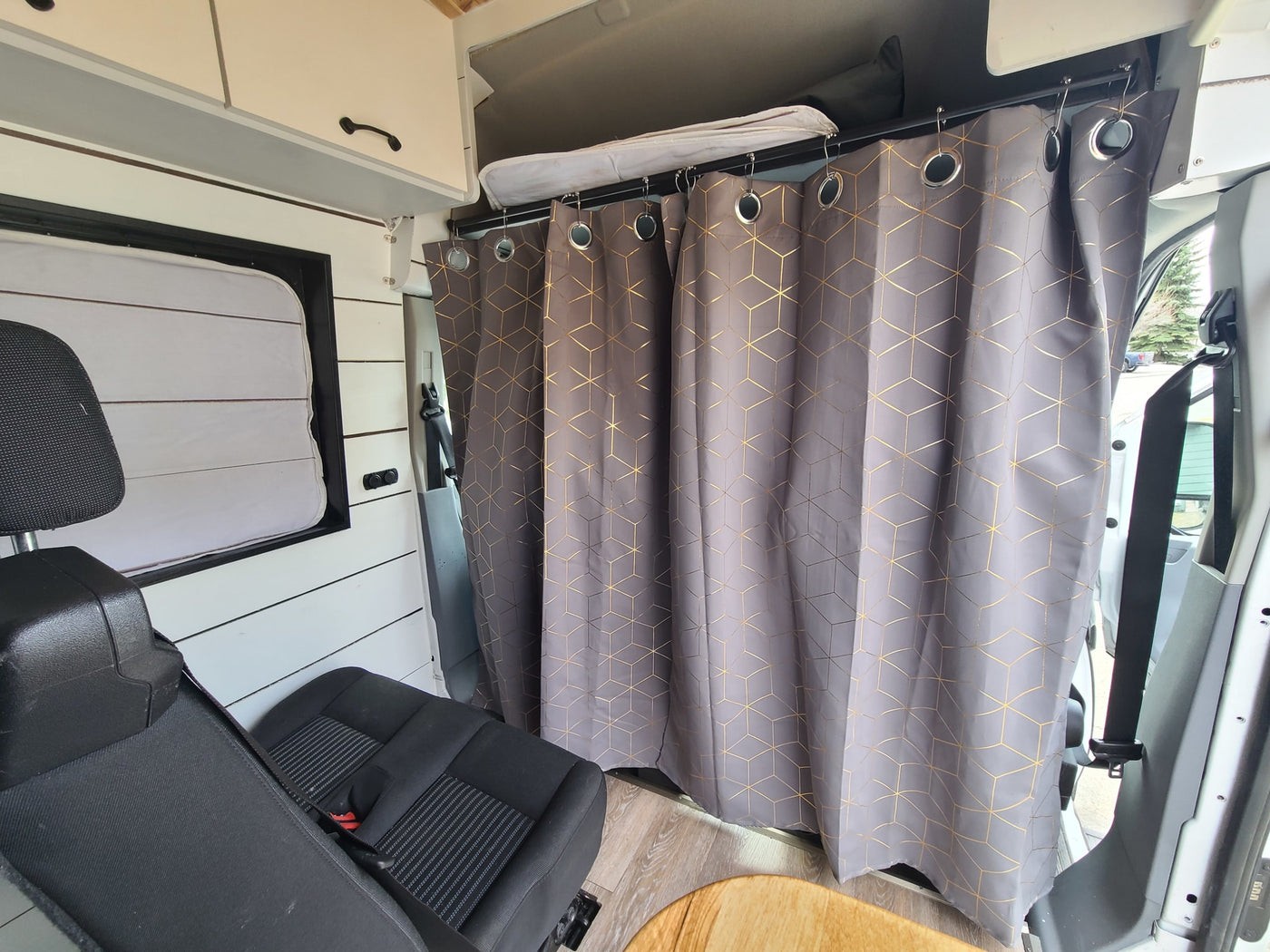Cozy RV rental interior: a grey and gold geometric privacy curtain hangs from a rod, next to a black seat and white cabinets. — photo 18