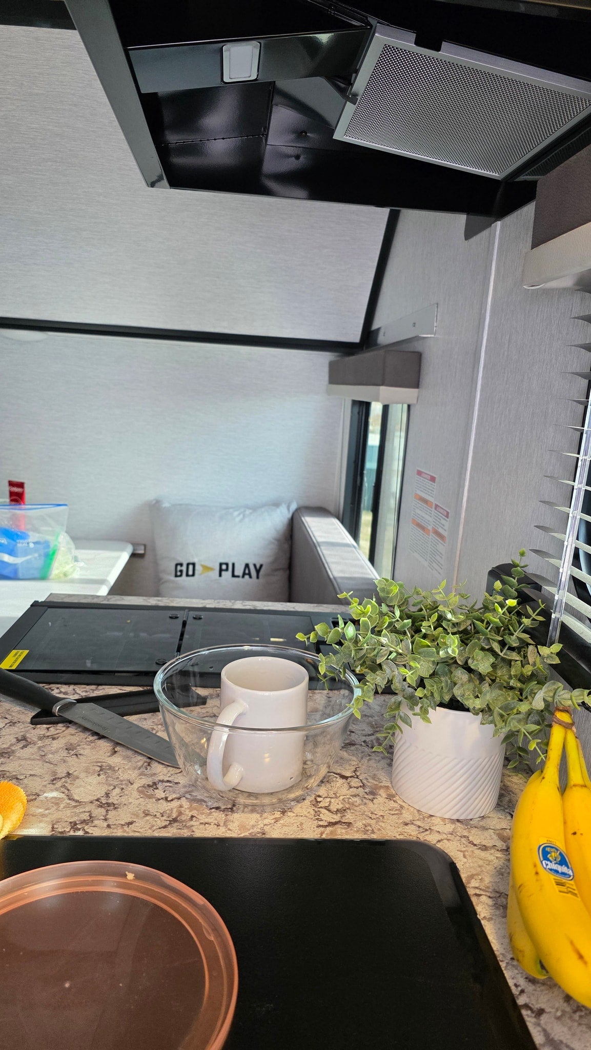 Cozy RV rental kitchen: compact stove, food prep counter with plant & bananas, and a dinette ready for your adventure. — photo 15