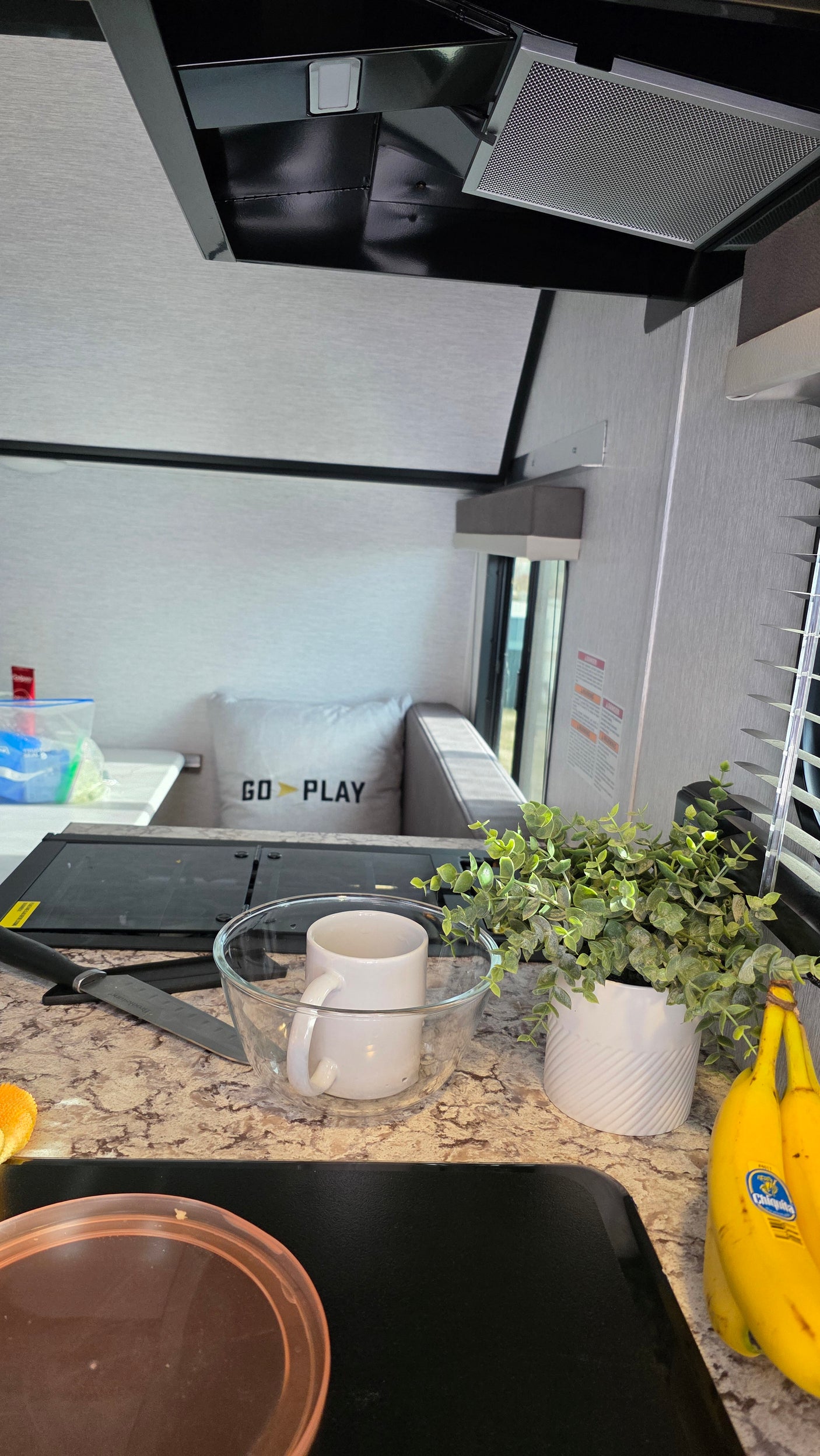 Cozy RV rental kitchen: compact stove, food prep counter with plant & bananas, and a dinette ready for your adventure.