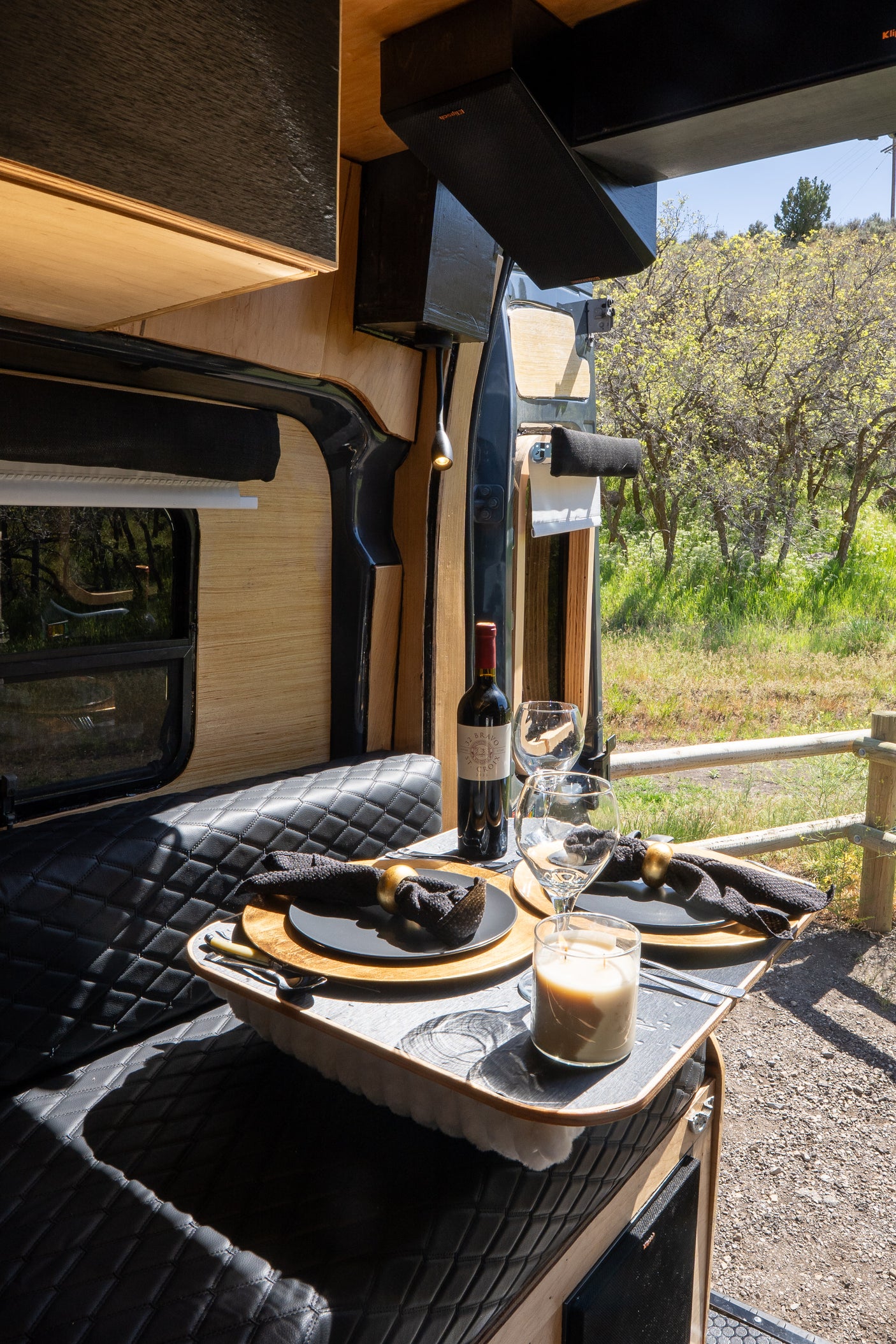 This rv rental offers a charming dining setup for two, complete with wine, in a cozy camper van with a scenic outdoor backdrop.