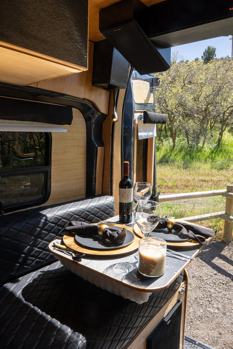 This rv rental offers a charming dining setup for two, complete with wine, in a cozy camper van with a scenic outdoor backdrop.