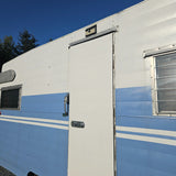 Close-up of a blue and white travel trailer's side, showing its entry door, windows, and a solar light. Consider this RV for rental.