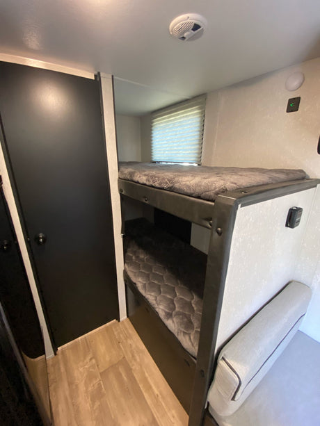 Compact RV rental interior featuring bunk beds, a door, and a comfy bench for efficient living.