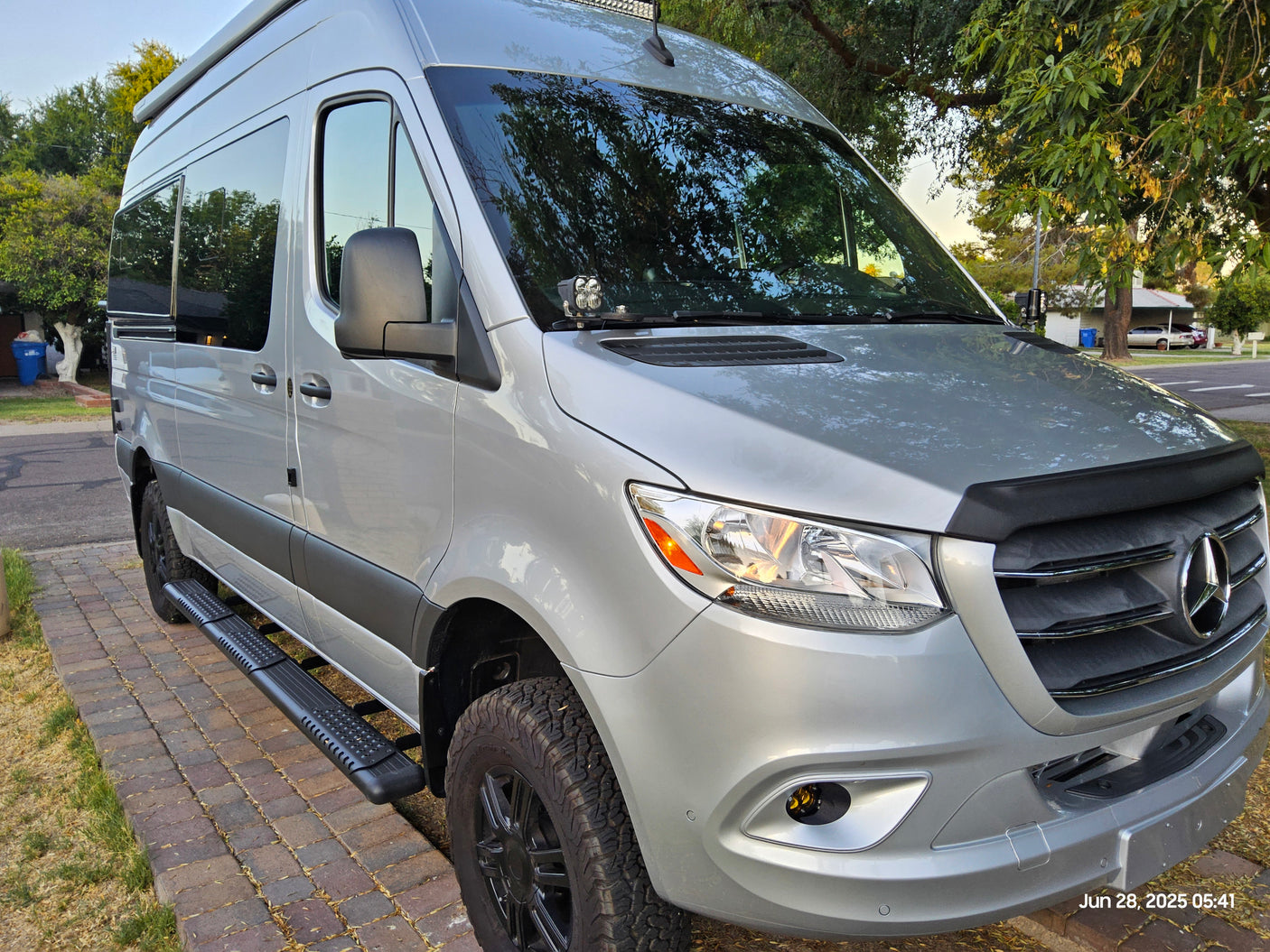 Silver Mercedes-Benz Sprinter RV rental: custom camper van with off-road tires and running boards, parked outside.