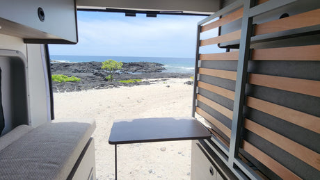 RV rental: Ocean, volcanic beach, and rugged coast visible from inside a camper van. Ideal for van life travel.