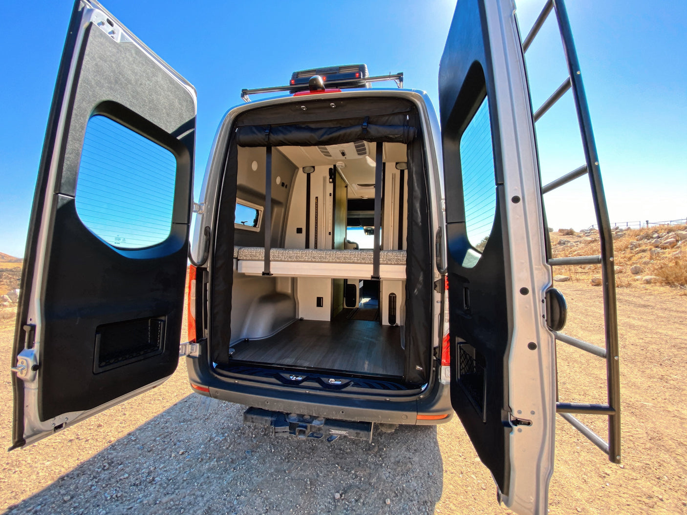 This RV rental's open rear doors showcase a versatile interior with a bunk bed and lower storage. Ready for your next adventure!