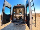 This RV rental's open rear doors showcase a versatile interior with a bunk bed and lower storage. Ready for your next adventure!