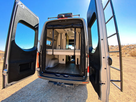 This RV rental's open rear doors showcase a versatile interior with a bunk bed and lower storage. Ready for your next adventure!