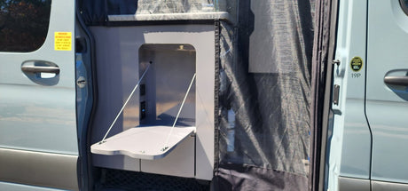 Interior of an RV rental van, featuring an open side door with a fold-down table and power outlets.