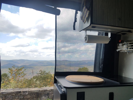 Stunning mountain view from an RV rental, showcasing the camper van's functional kitchen counter, cooktop, and paper towel holder.