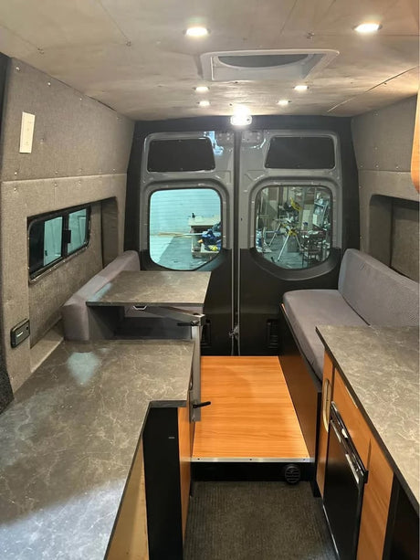 Modern rv rental van conversion interior: gray walls, dark countertops, a dinette, and a versatile bed/seating area.