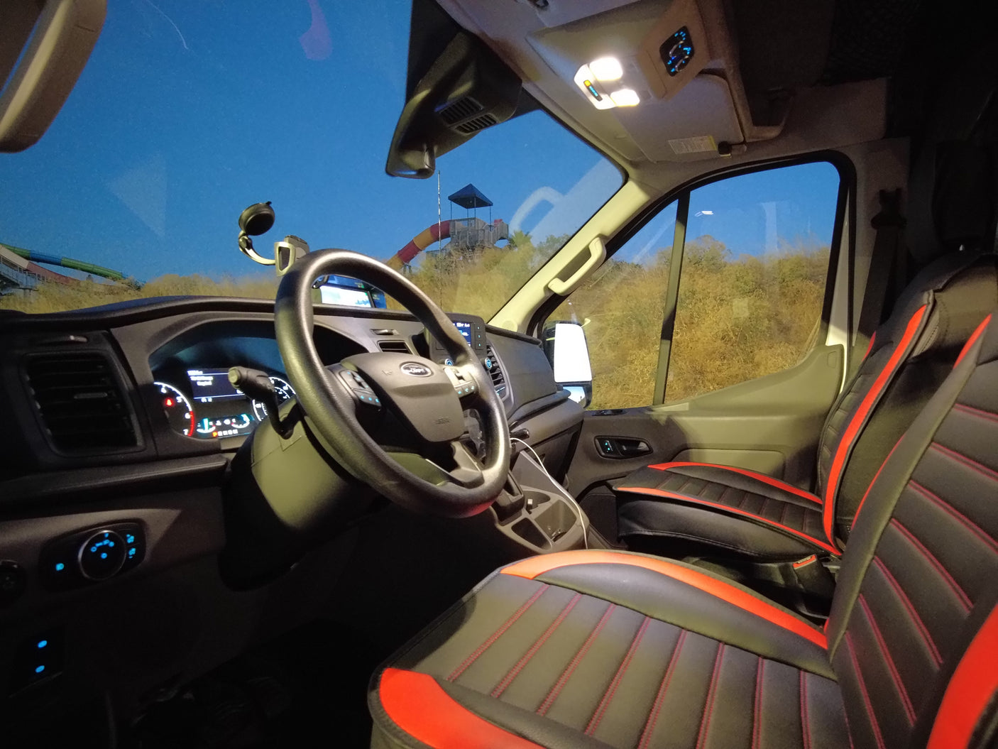 **RV rental** van interior with red & black seats, showing the dashboard & view of water park slides.