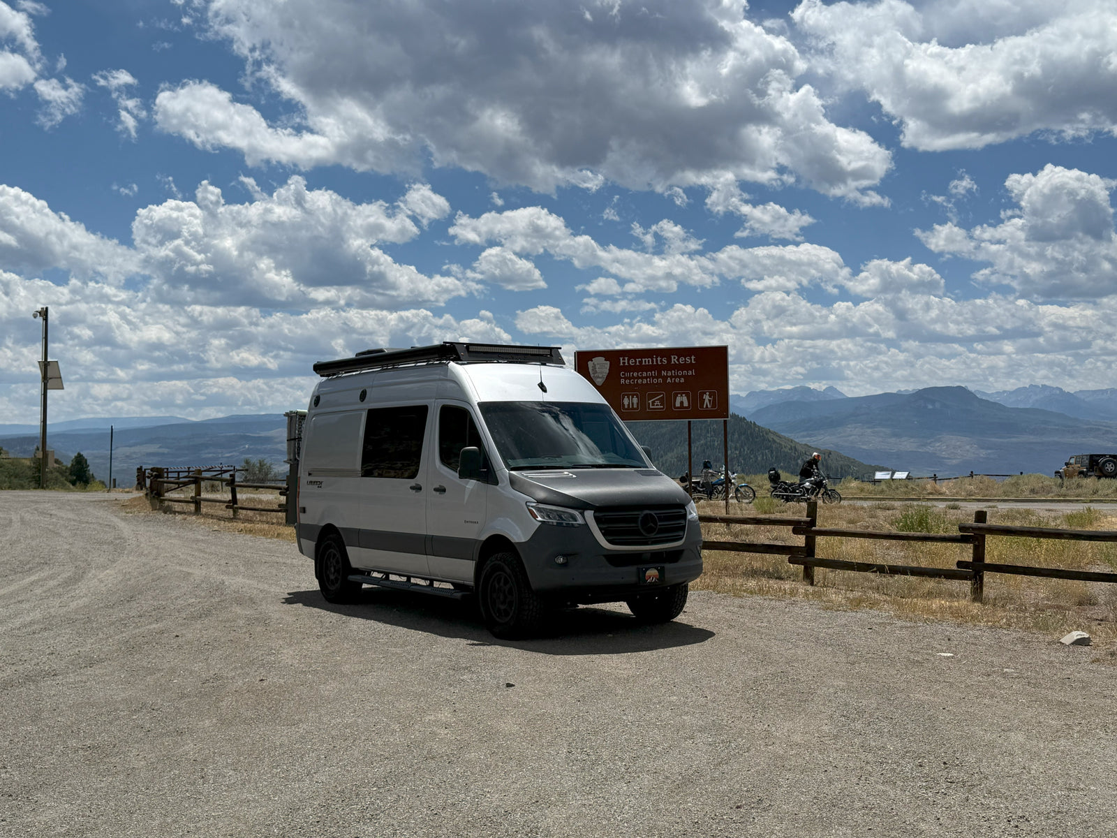 White RV rental (Sprinter van) at Hermits Rest, Curecanti National Recreation Area, offering scenic mountain views under cloudy skies.
