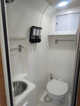 This clean, compact bathroom in an RV rental includes a toilet, small sink, shower, and wall-mounted shampoo/soap dispensers.