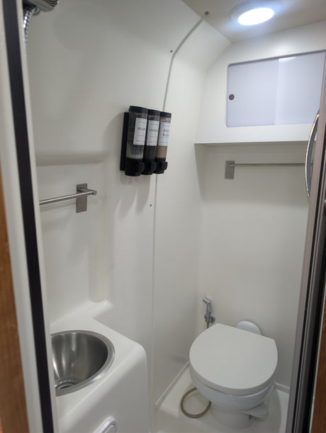 This clean, compact bathroom in an RV rental includes a toilet, small sink, shower, and wall-mounted shampoo/soap dispensers.