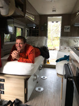Man smiles from a comfortable bed in an RV rental, overlooking a scenic outdoor view. Ideal for travel and relaxation.