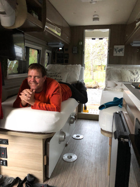 Man smiles from a comfortable bed in an RV rental, overlooking a scenic outdoor view. Ideal for travel and relaxation.