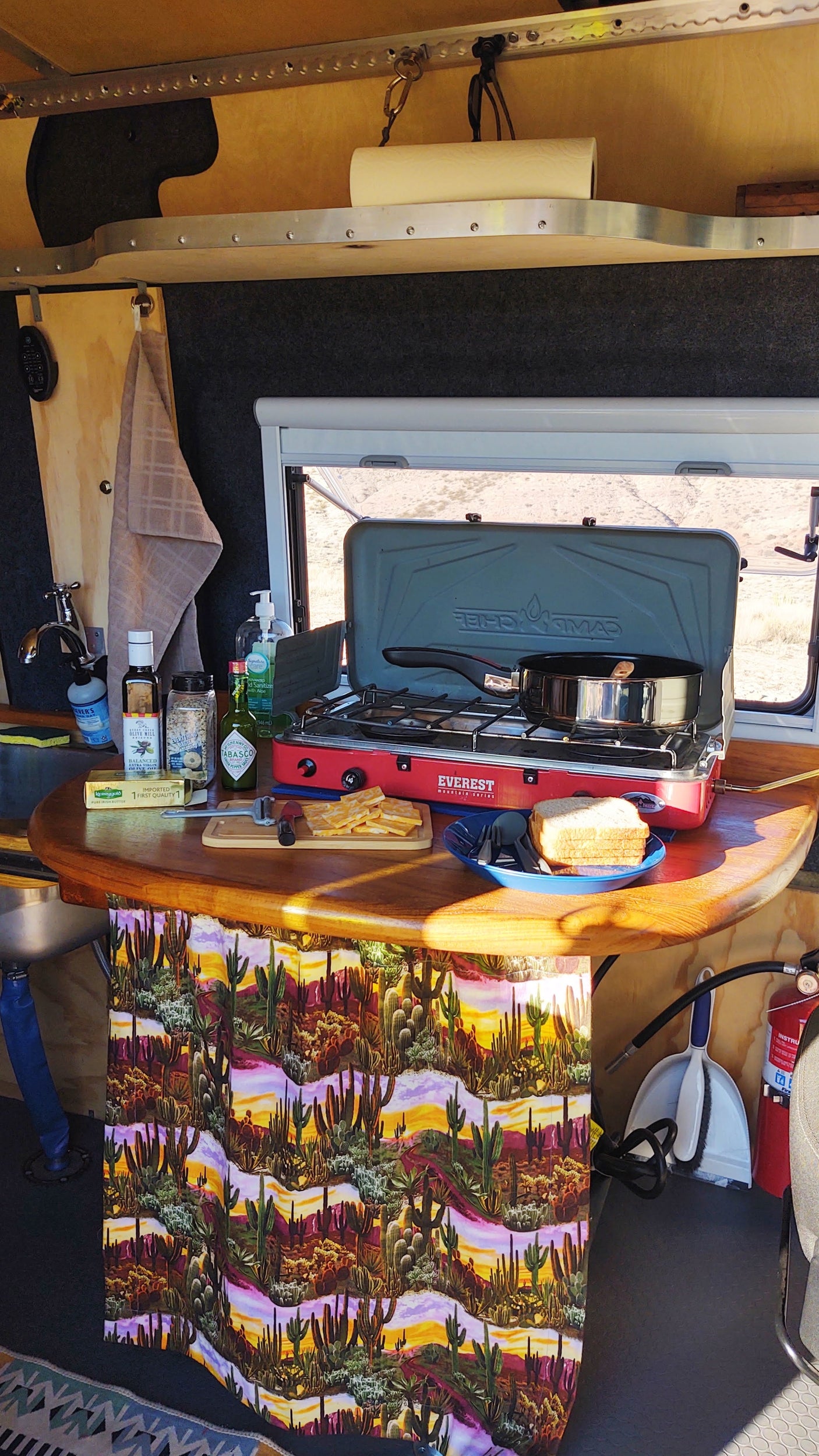 This RV rental's functional kitchen boasts a portable stove, sink, supplies, and a scenic desert window view.