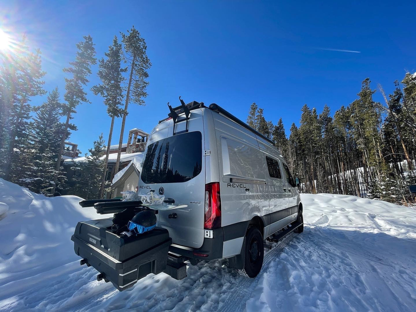 Silver Winnebago Revel RV rental in snowy mountains, equipped with skis & snowboard for winter adventure.