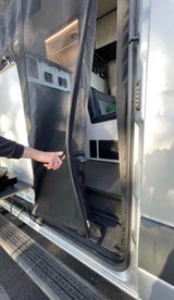 RV rental: Hand opens a black mesh screen door on a camper van, revealing the modern interior with seating & storage.